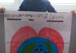 Uczeń trzyma wykonany przez siebie plakat. Przedstawia on kulę ziemską oraz napis: Środowisko ponad wszystko.